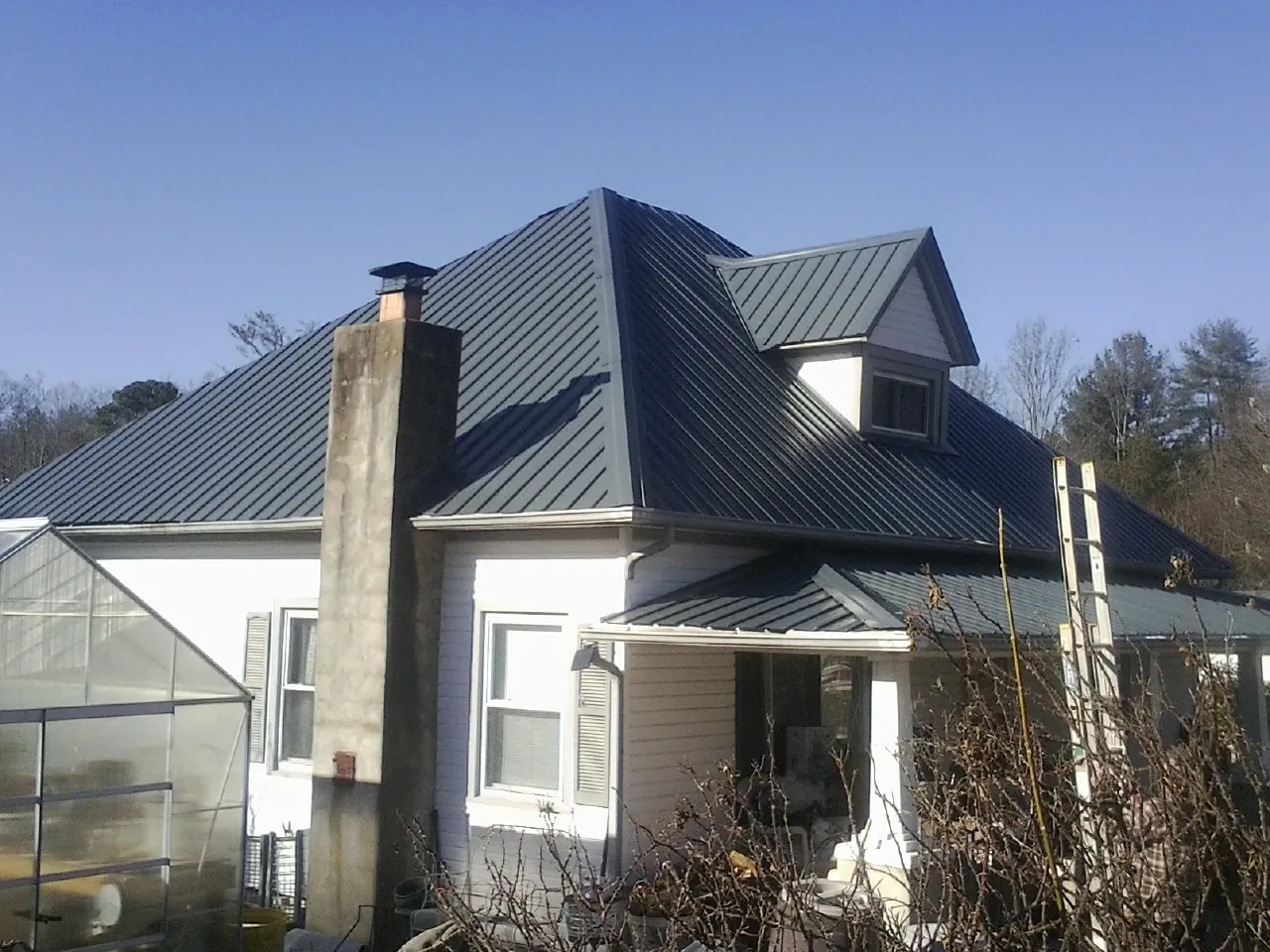 Dark blue standing seam metal roof on a white farmhouse with dormer — Slate & Tile Roof Repair by Roofing Brothers in Conner