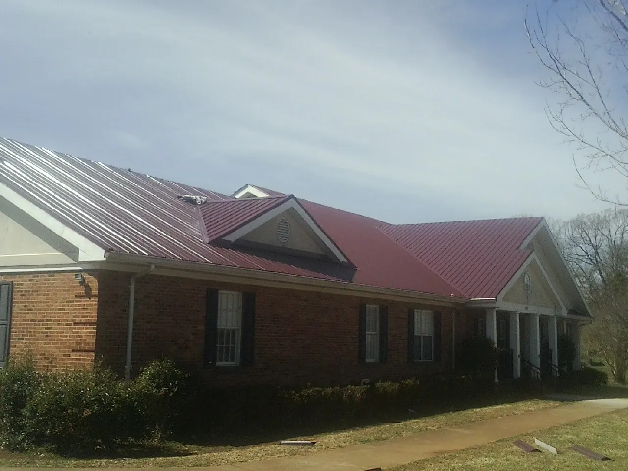 Red metal roof with gabled entries on a long brick building, from a Hail Damage Roof Repair job in Conner