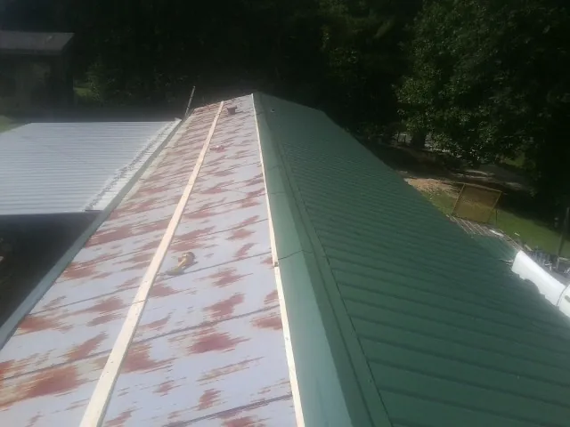 Old rusted panels beside newly installed green metal roofing — Wind Damage Roof Repair by Roofing Brothers in Conner