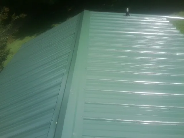 New green metal panels meeting at the ridge of a roof — Flat Roof Repair work by our crew in Conner
