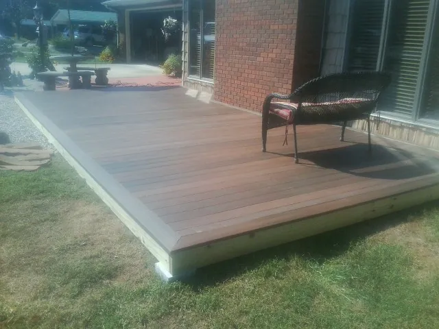 New wood deck and wicker chair beside a brick house in Conner