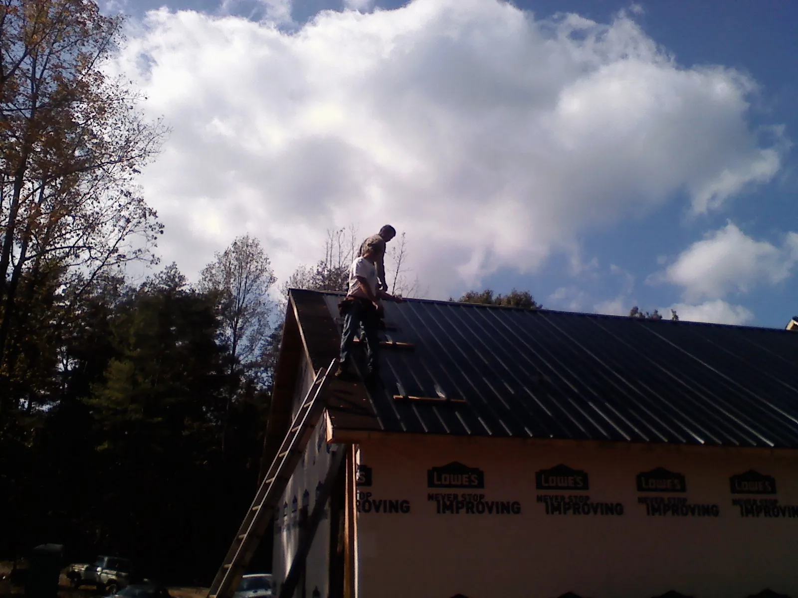 Roofer fastening dark metal panels high against a cloudy sky, from a Roof Inspection job in Conner