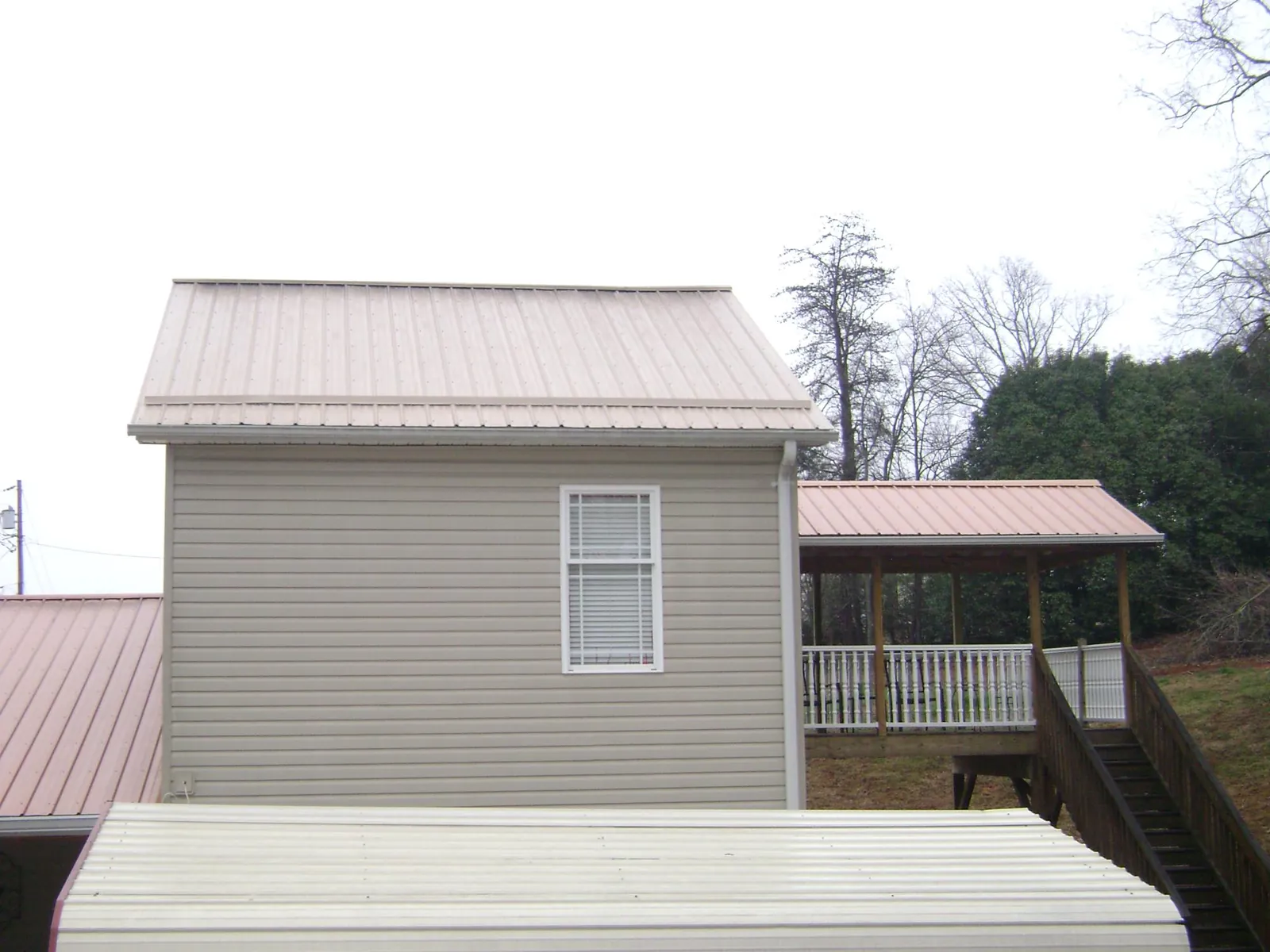 Tan metal roofs on a two story addition and attached porch, from a Roof Replacement job in Conner